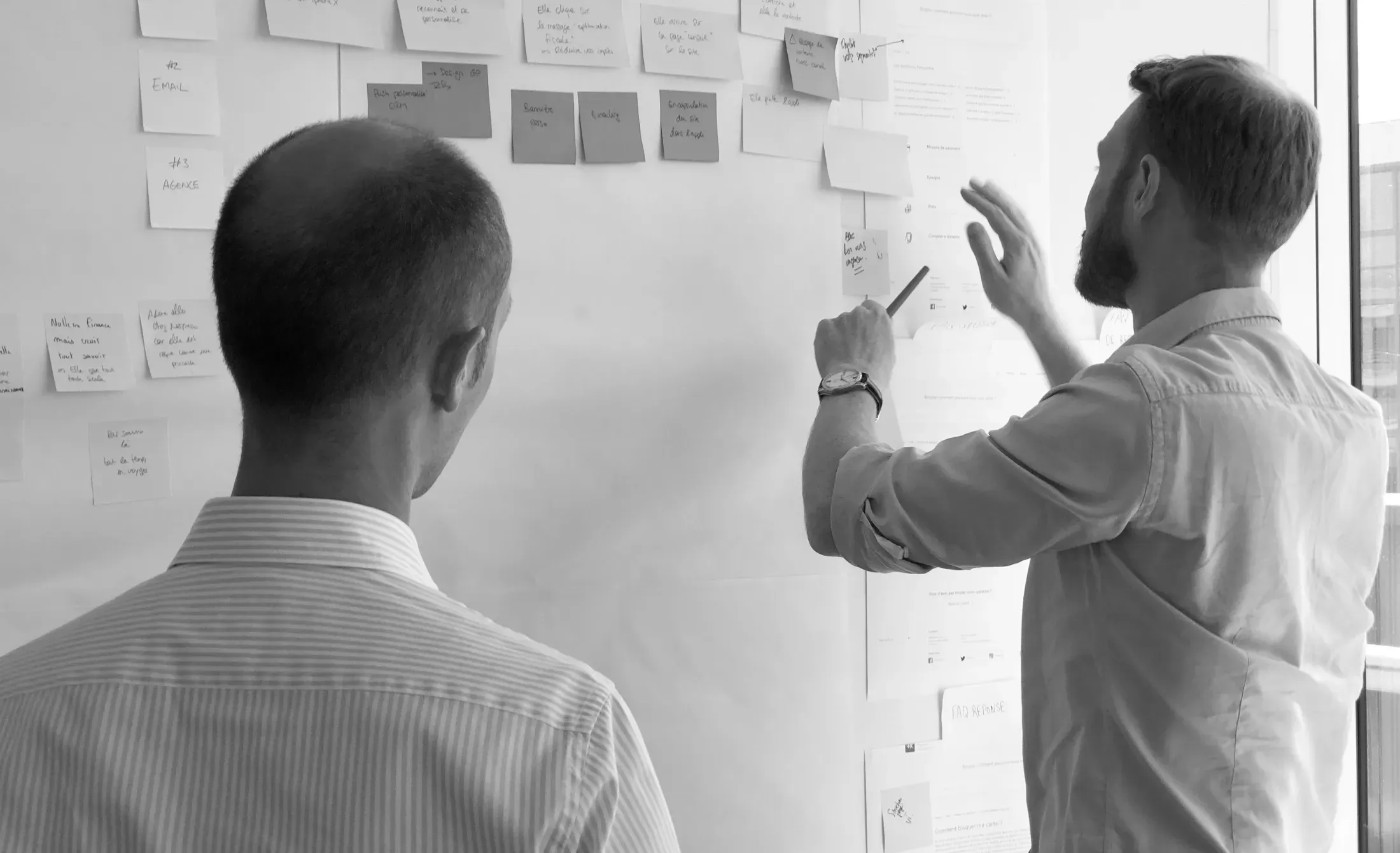 Deux collaborateurs consignant leurs observations sur un mur de post-it